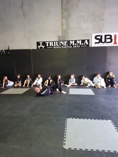 Kids lined up under the TRIUNE wall, coach demonstrating